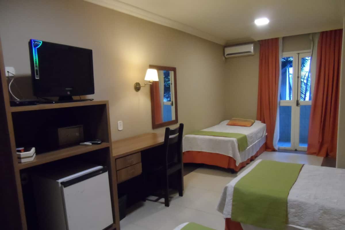 A hotel room with a desk, a television, a bed, a chair, and an air conditioning unit.