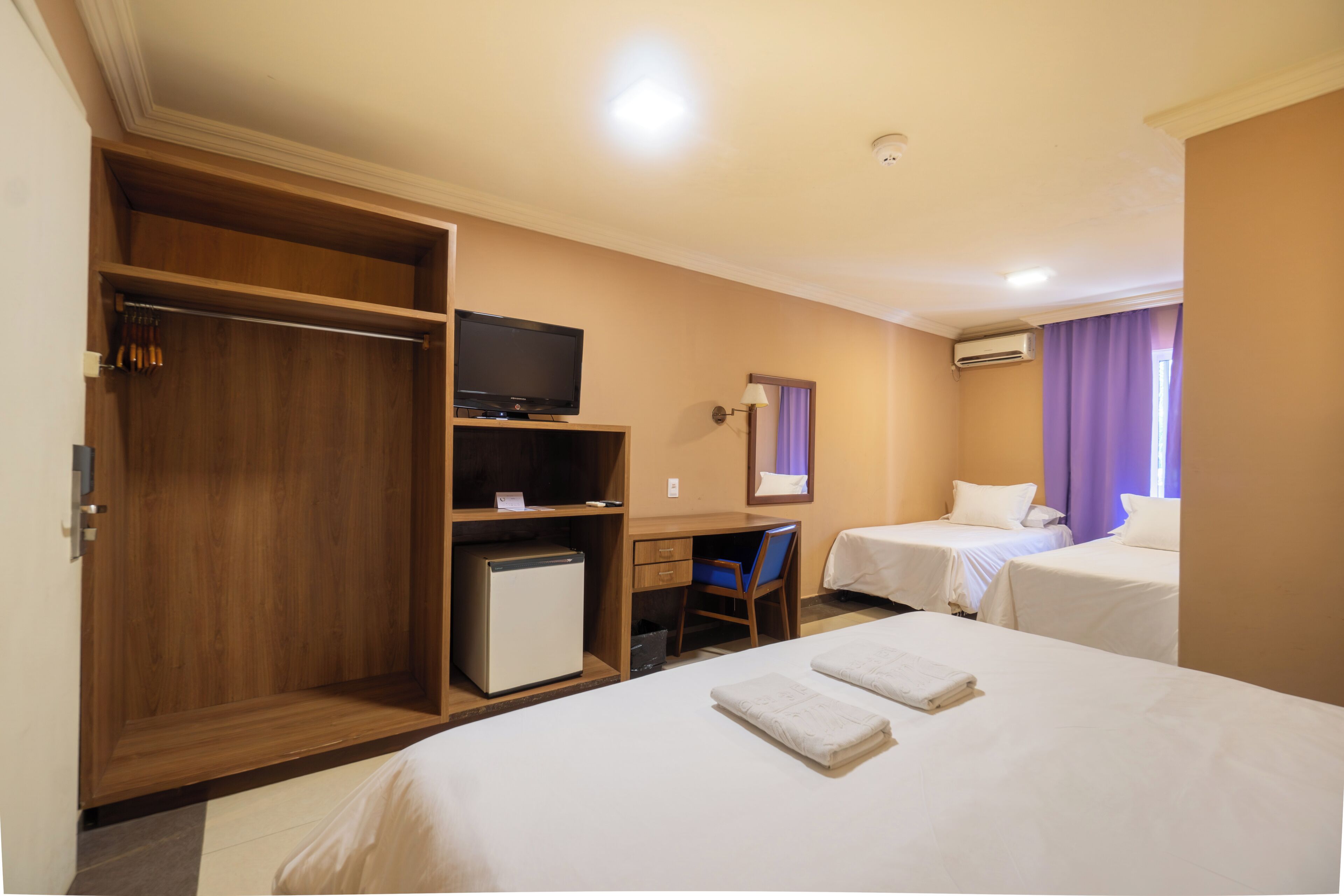 A hotel room with two beds, a desk with a computer, a television, and a wardrobe.