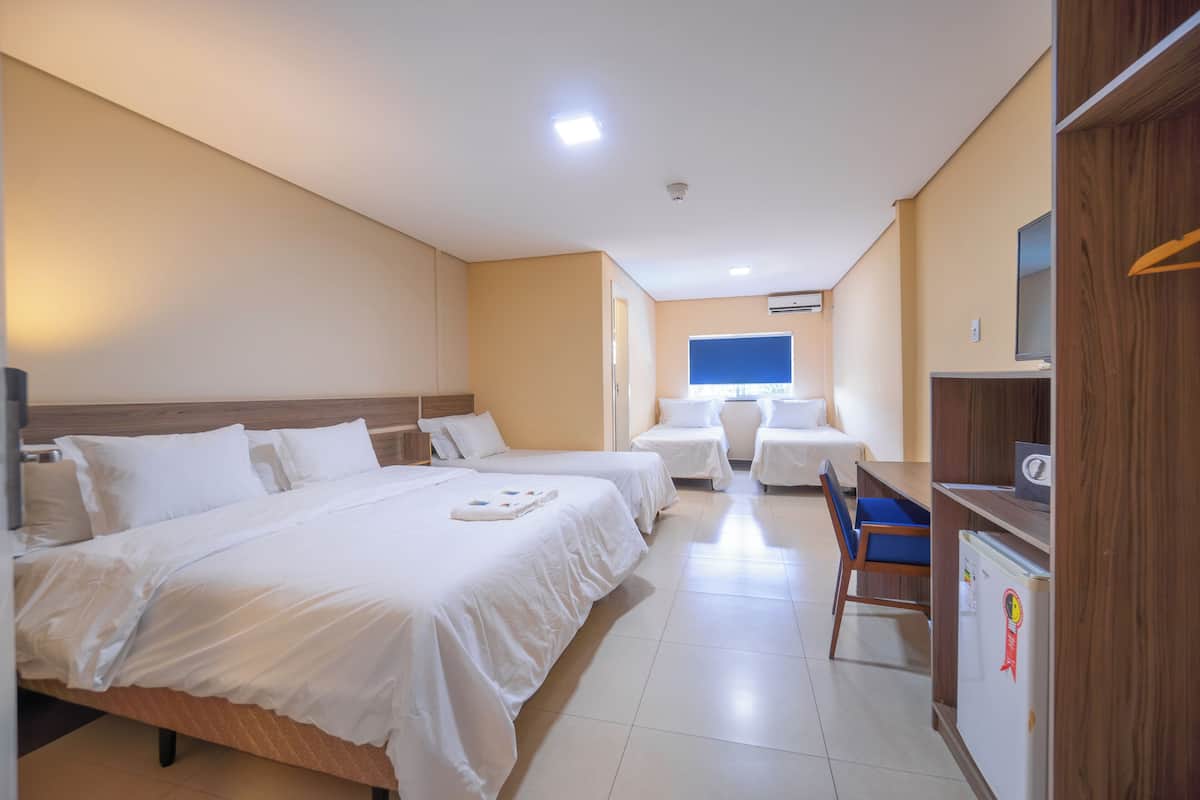 A hotel room with two beds, a desk, a chair, a TV, and a refrigerator.