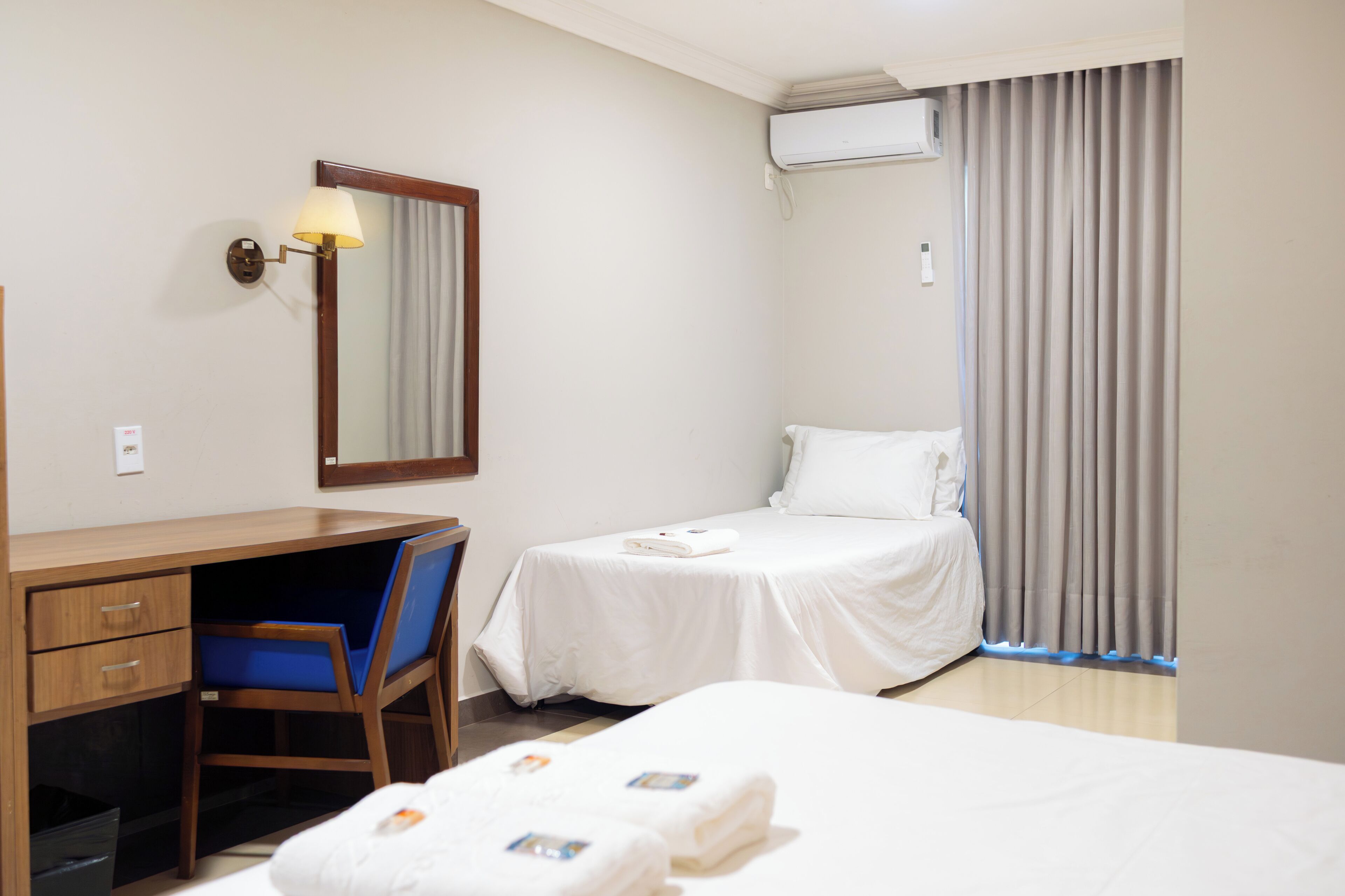 A hotel room with a desk, two beds, a chair, and an air conditioning unit.