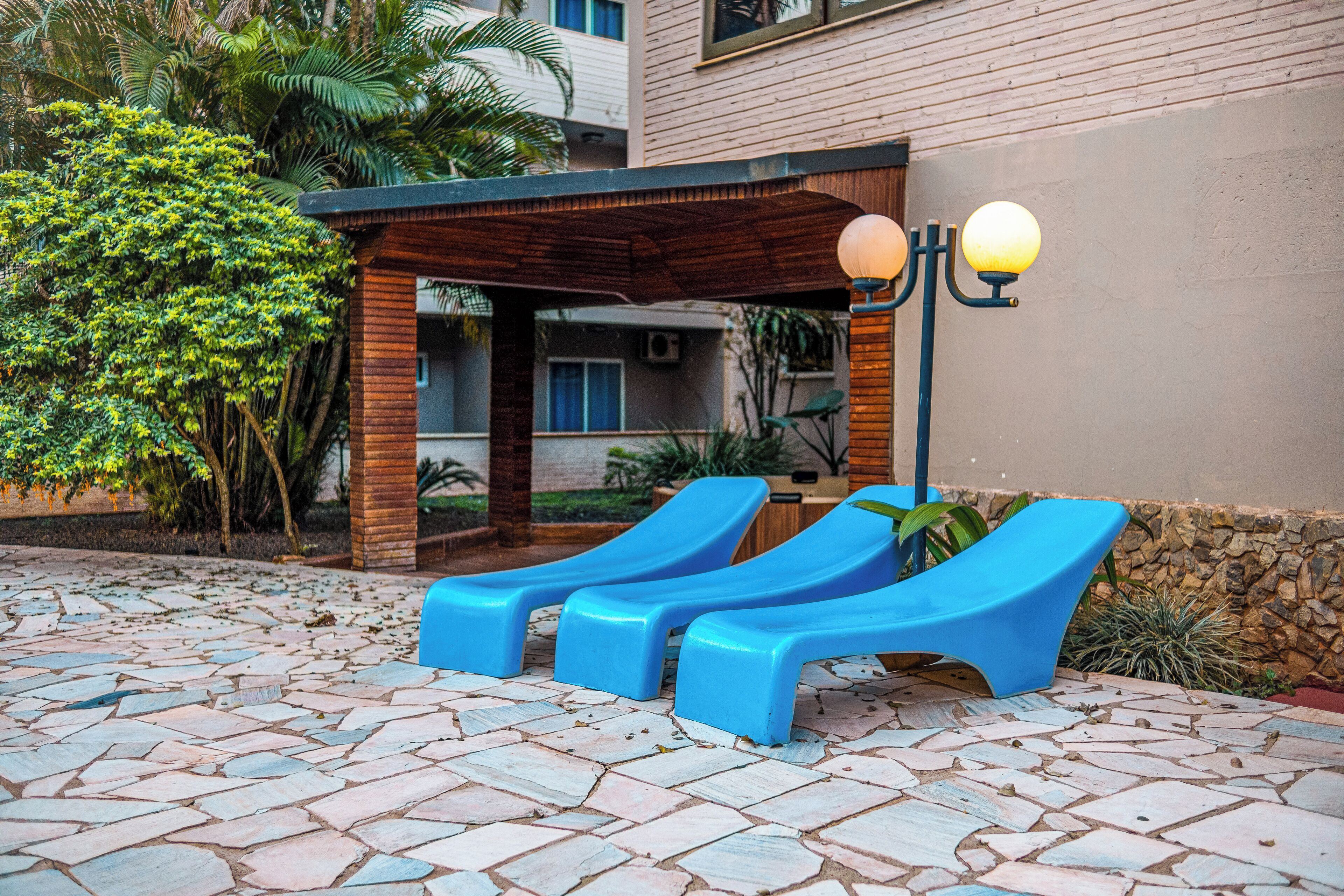 A covered outdoor seating area with two blue lounge chairs and a wall-mounted lamp.