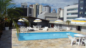 Un espace piscine aménagé sur le toit, avec des chaises longues, des parasols et une vue sur les bâtiments environnants.