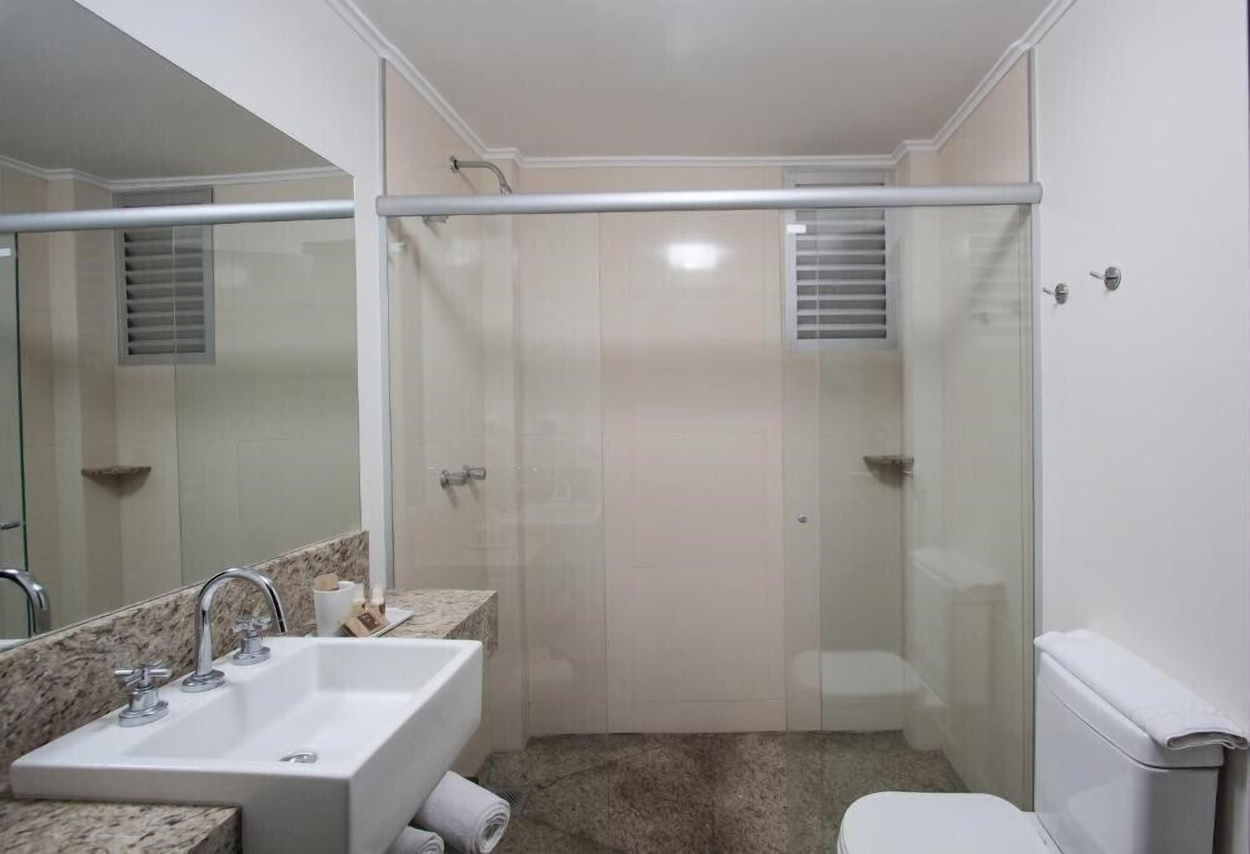A bathroom with a glass-enclosed shower, a sink with a marble countertop, and a toilet.