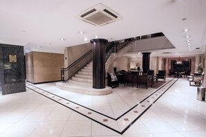 Eine geräumige Lobby mit einer imposanten Treppe, einem Empfangsbereich und einer Sitzecke.