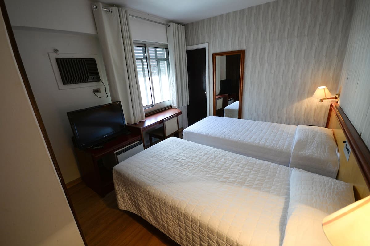 A hotel room with two beds, a desk with a television, a mirror, and a lamp.