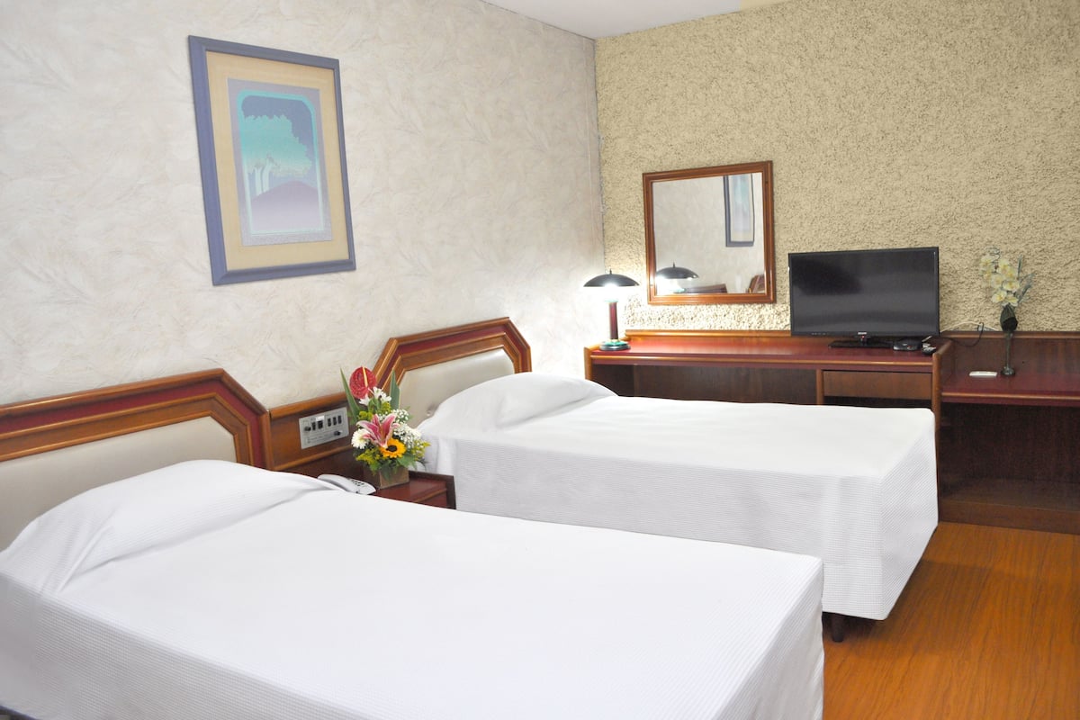A hotel room with two beds, a TV, a desk with a lamp, and a mirror.