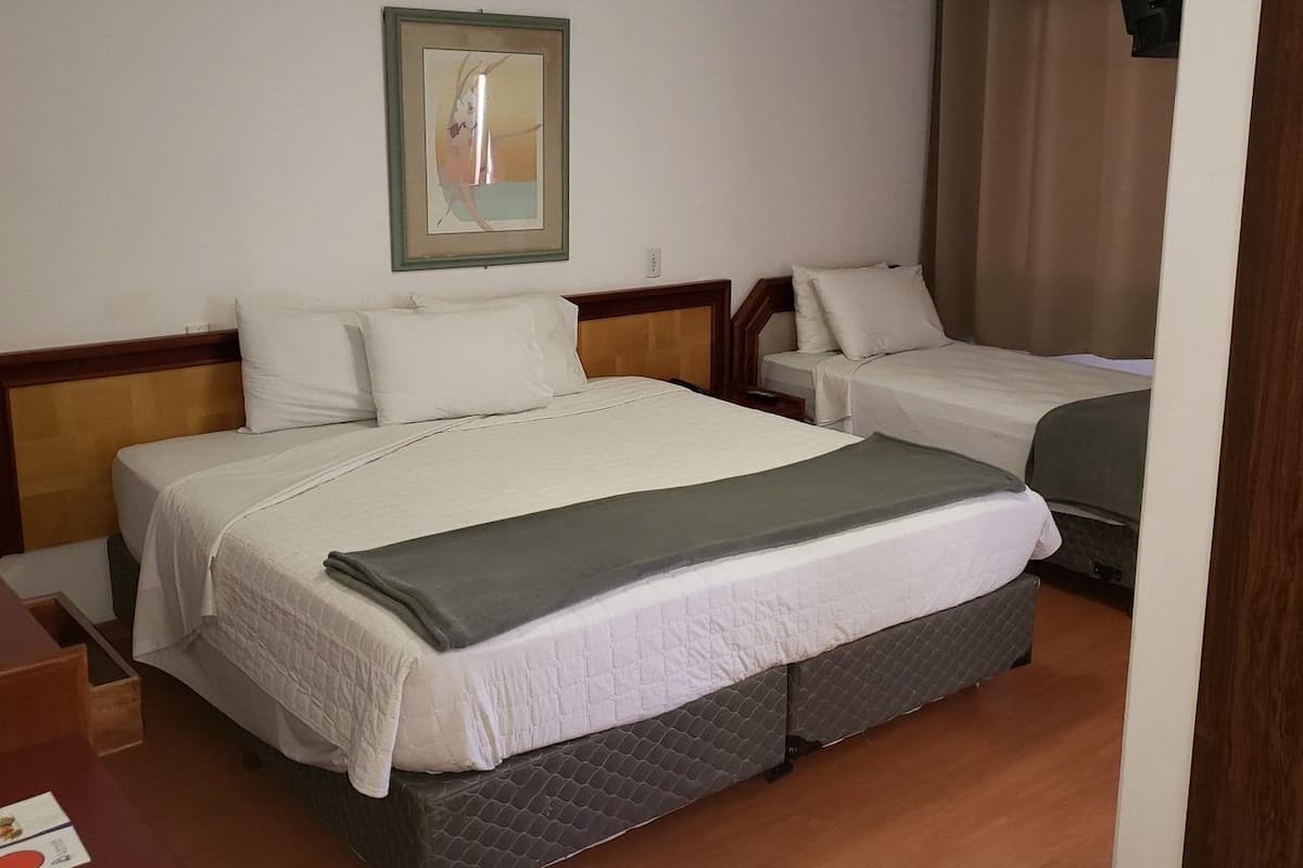 A hotel room with a large bed, a smaller bed, a wooden headboard, a bedside table, and a framed picture on the wall.