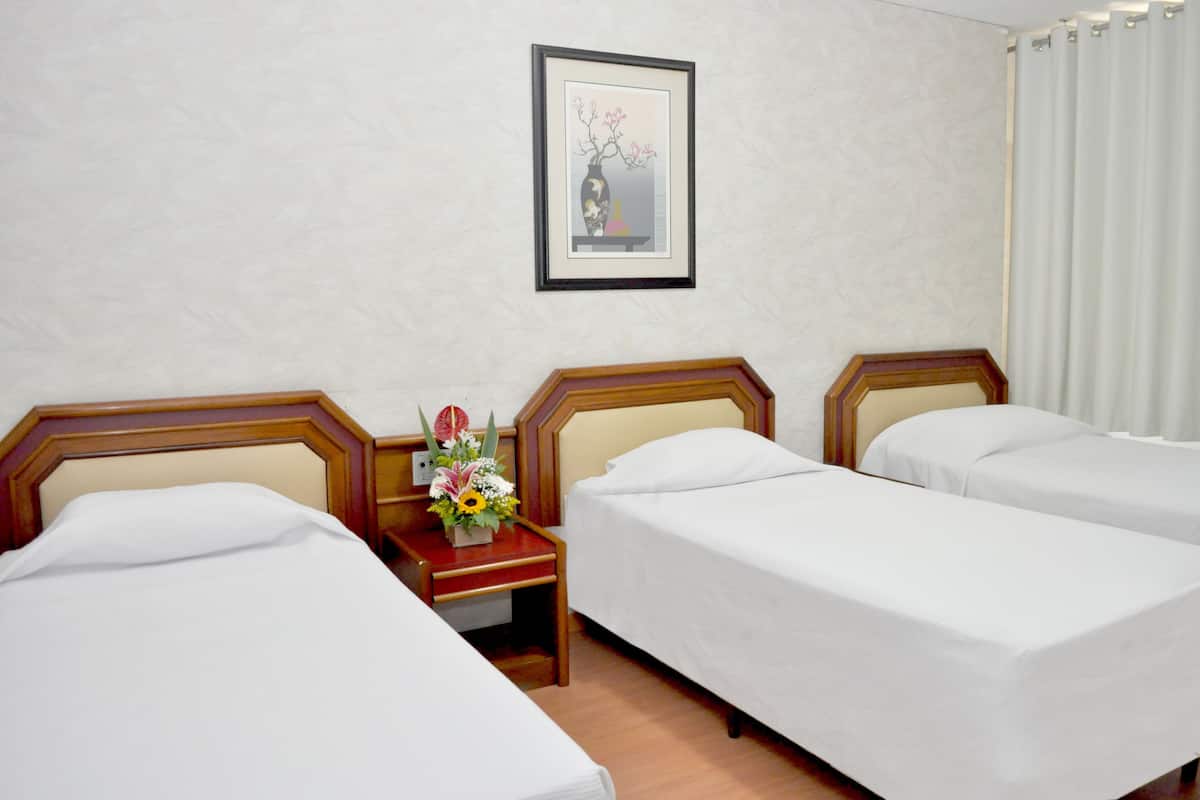 A hotel room with two single beds, a wooden nightstand with a vase of flowers, and a framed picture on the wall.