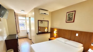 A hotel room with a bed, bedside table, lamp, air conditioning unit, TV, and a window with curtains. - Lira Hotel (Curitiba)