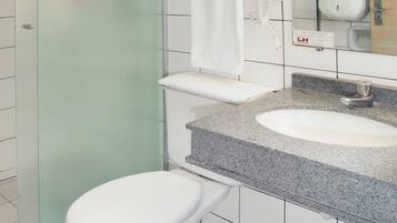 A bathroom with a glass shower enclosure, a white toilet, a granite countertop sink, and a mirror above the sink.