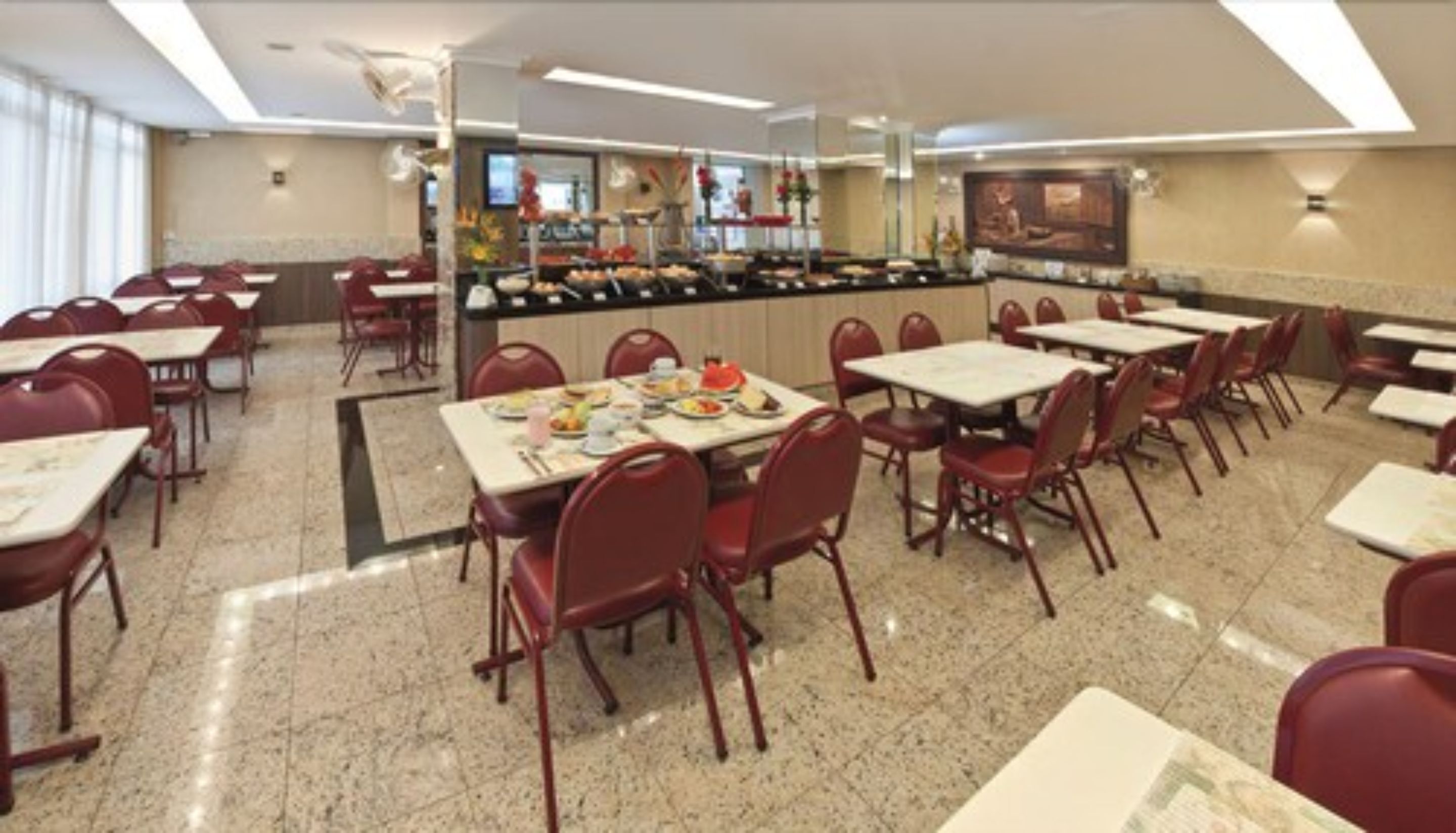 A dining area with tables and chairs, a buffet counter, and a large painting on the wall.