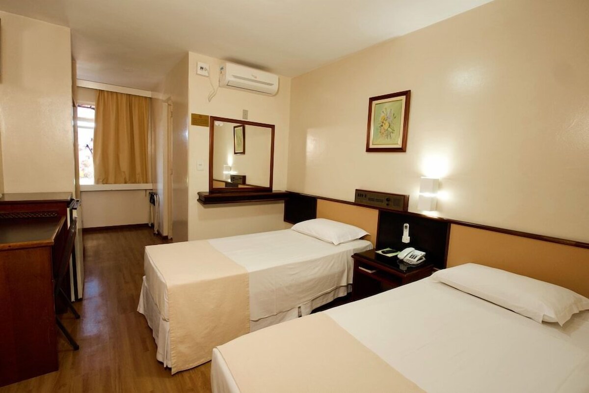 A hotel room with two beds, a desk, a telephone, and an air conditioning unit.