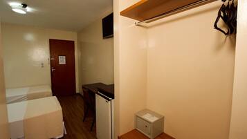 Una habitación pequeña con cama, escritorio, refrigerador y un mueble bajo.