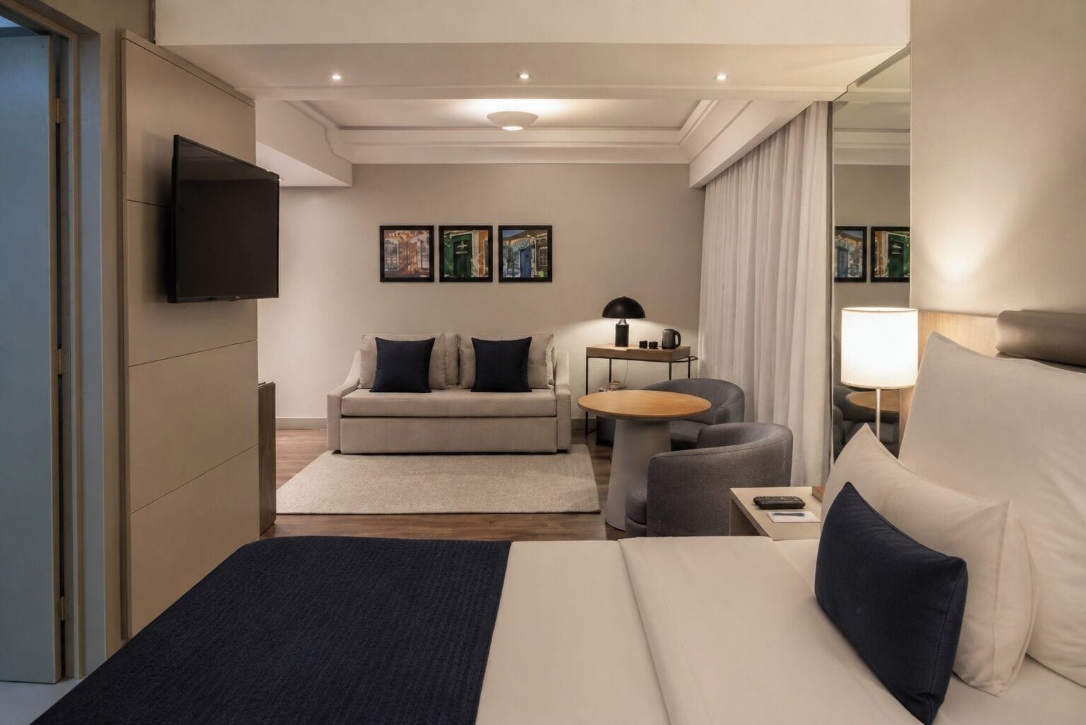 Habitación de hotel con cama, sofá, una pequeña mesa redonda, escritorio y televisor montado en la pared.
