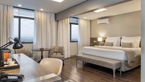 A modern hotel room with a large bed, a desk with a telephone, a chair, and a small table. - Blue Tree Premium Florianopolis (Florianópolis)