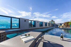 Area piscina moderna con vista sul mare, una sedia a sdraio e una bottiglia di vino.