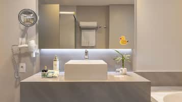 A modern bathroom with a large mirror, a sink, a hairdryer, and a potted plant.