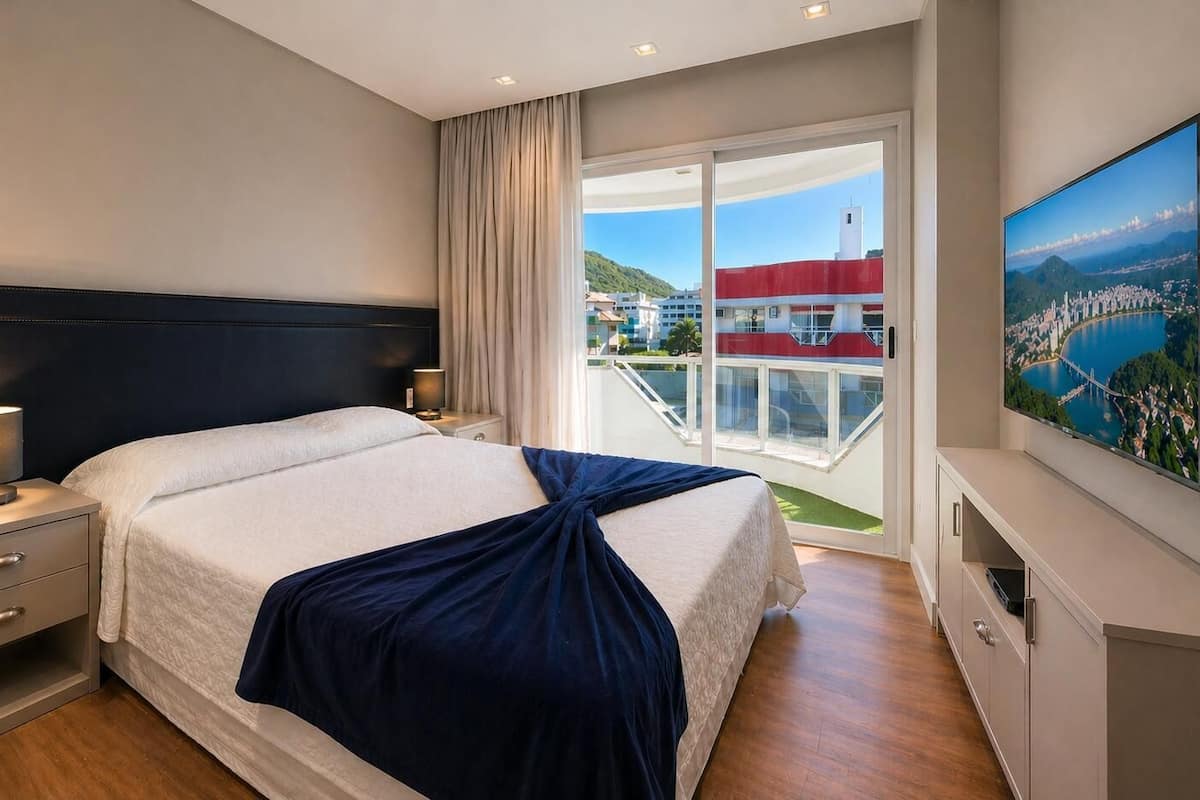 A hotel room with a bed, bedside tables, a TV, and a balcony with a city view.