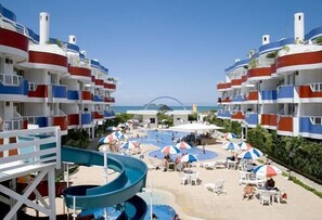 A resort with multiple balconies, a pool area with umbrellas, and a water slide. - Hotel Ingleses Holiday (Florianopolis)