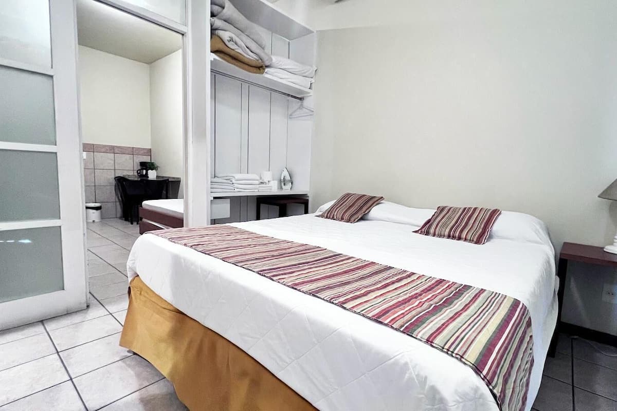 A hotel room with a bed, a nightstand, a lamp, a wardrobe, and a bathroom visible through an open door.