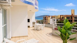 A balcony with white chairs, a potted plant, and a view of the sea and buildings. - Hotel Ingleses Holiday (Florianopolis)