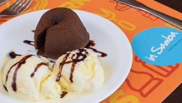 Un plato con pastel volcán de chocolate y helado de vainilla, servido sobre una fuente blanca con un logotipo azul.