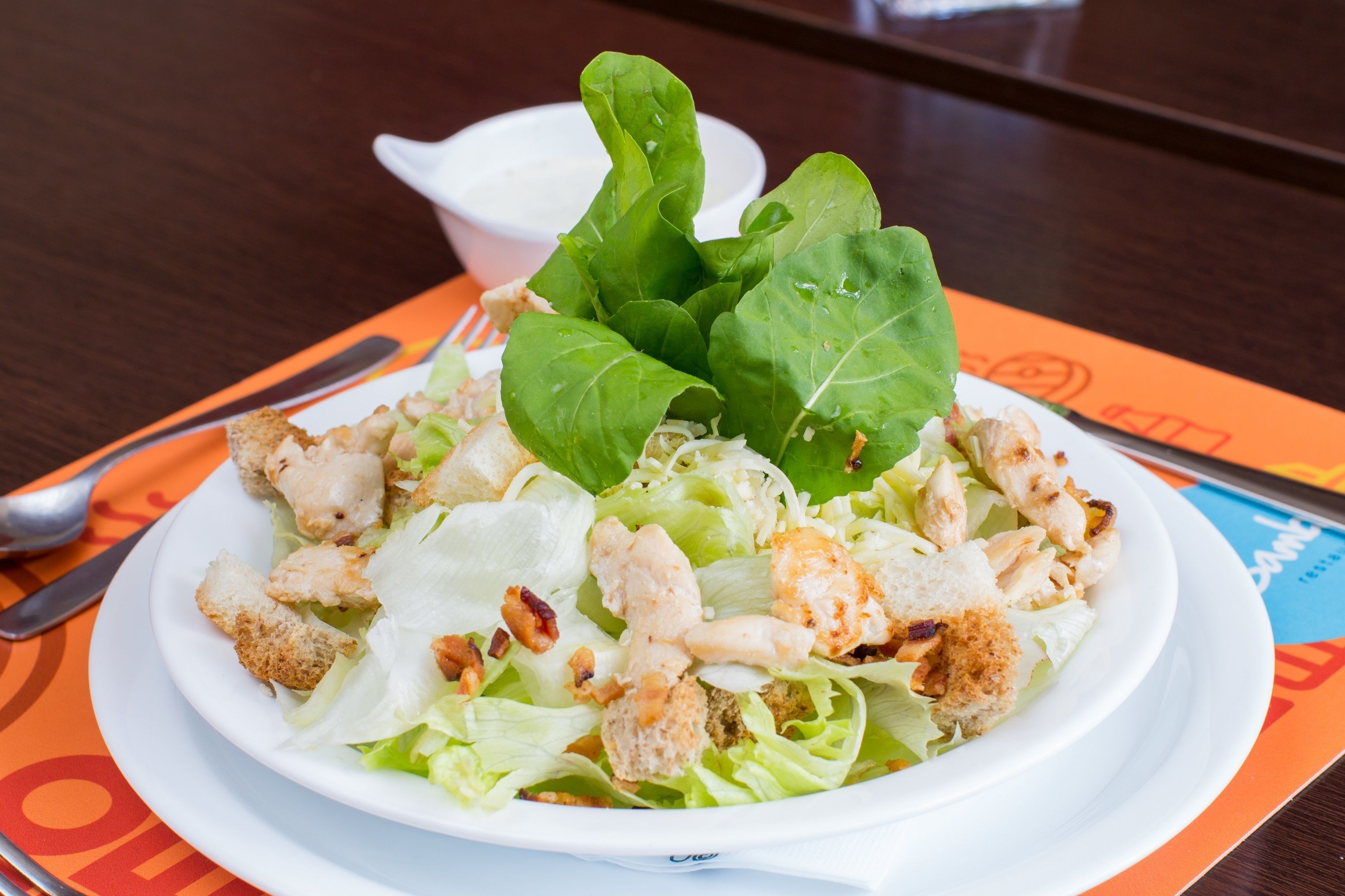 Ensalada con crutones y pollo, sobre un plato blanco, colocada sobre una mesa con camino de mesa.