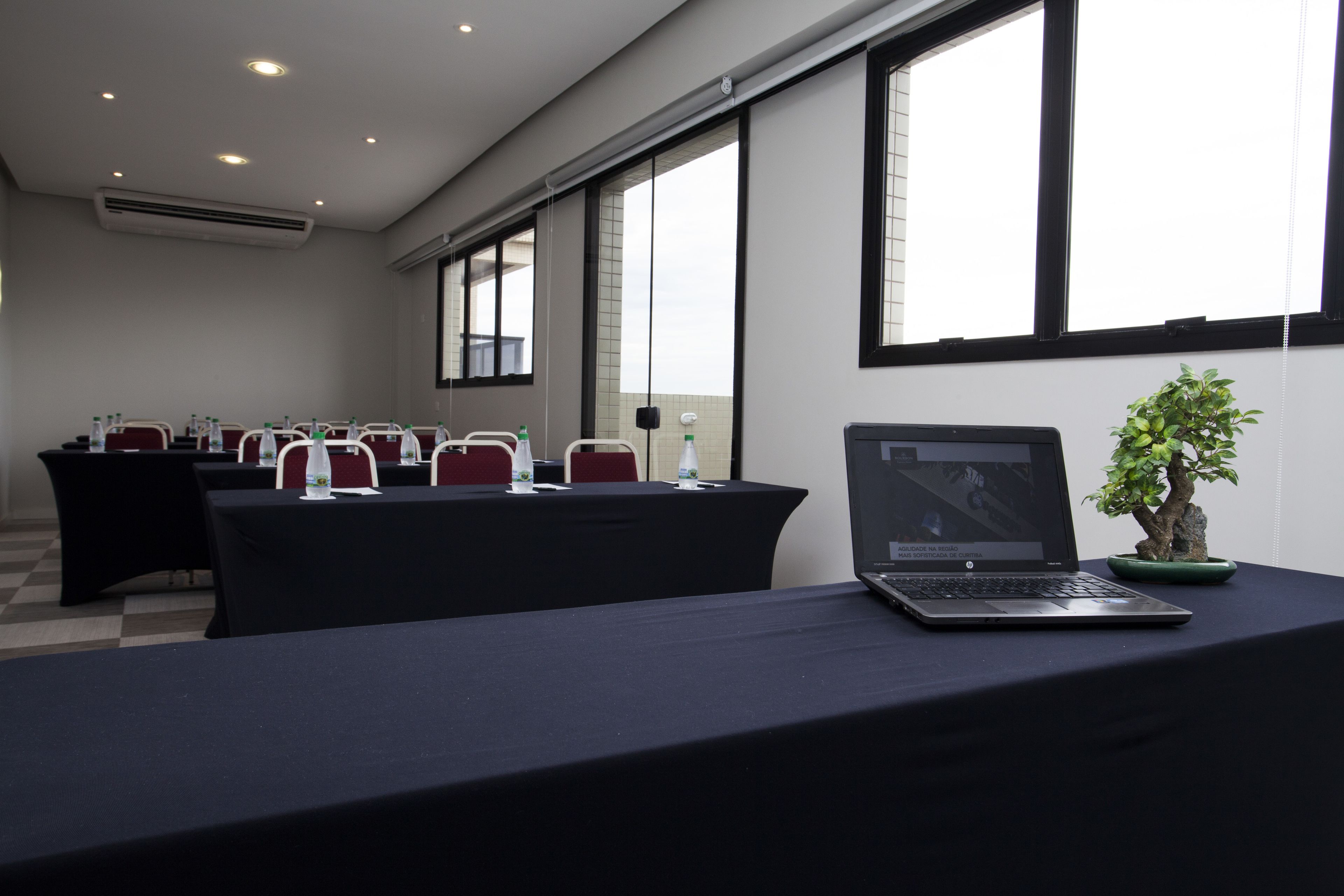Una sala de conferencias con mesas, sillas, una computadora portátil y una planta en maceta.