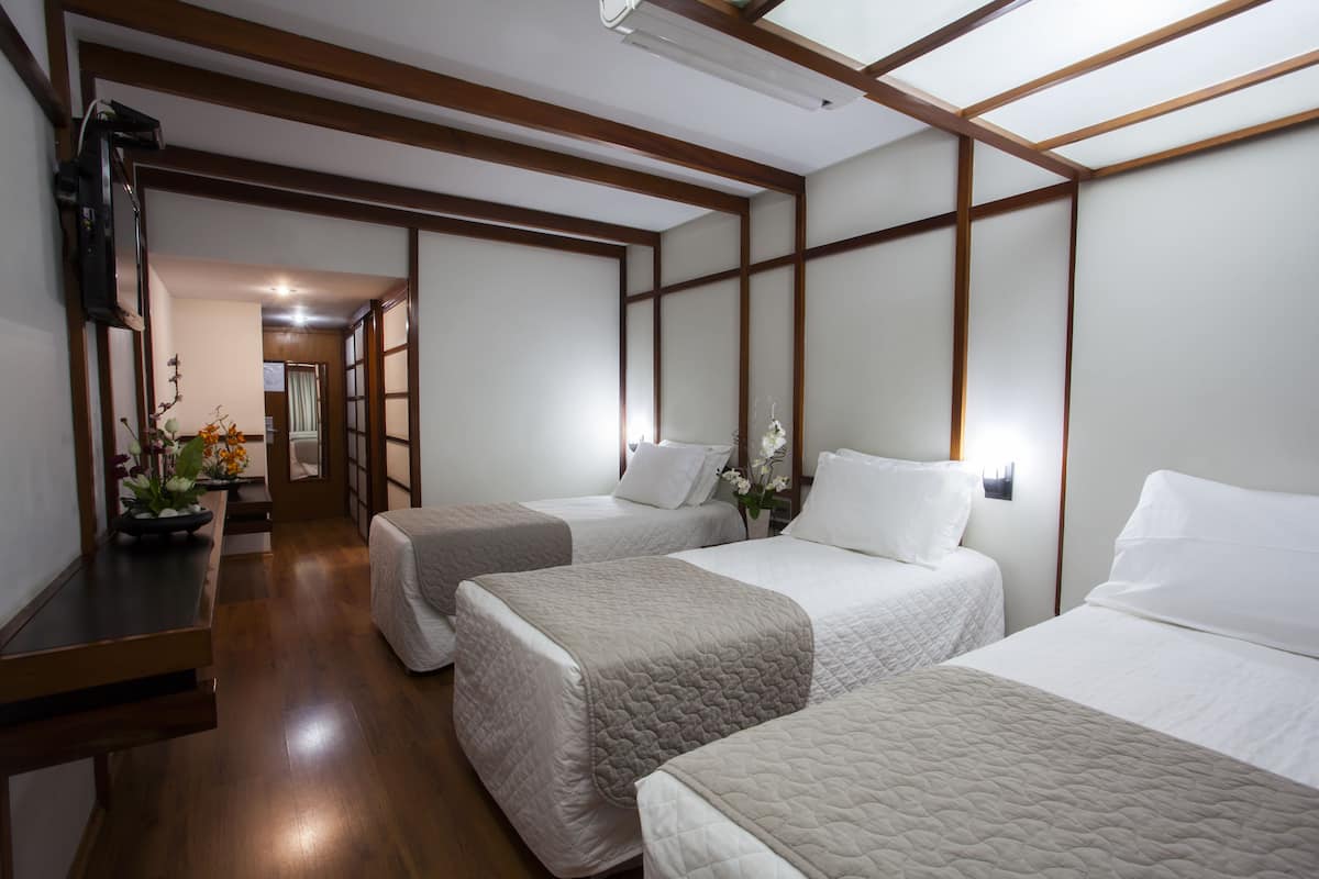 Une chambre d’hôtel avec trois lits, un plancher en bois et un décor intérieur de style japonais traditionnel.