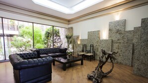 Un salon moderne avec un canapé en cuir noir, une table basse en verre et une sculpture en bois qui sert d’élément décoratif central.