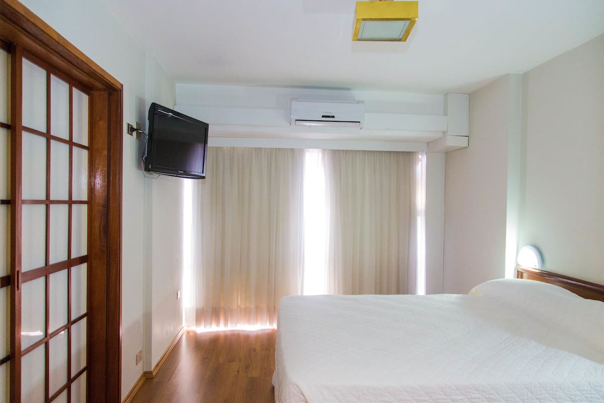 Une chambre d’hôtel équipée d’un lit, d’un téléviseur fixé au mur, d’un appareil de climatisation et d’une porte coulissante à motifs géométriques.