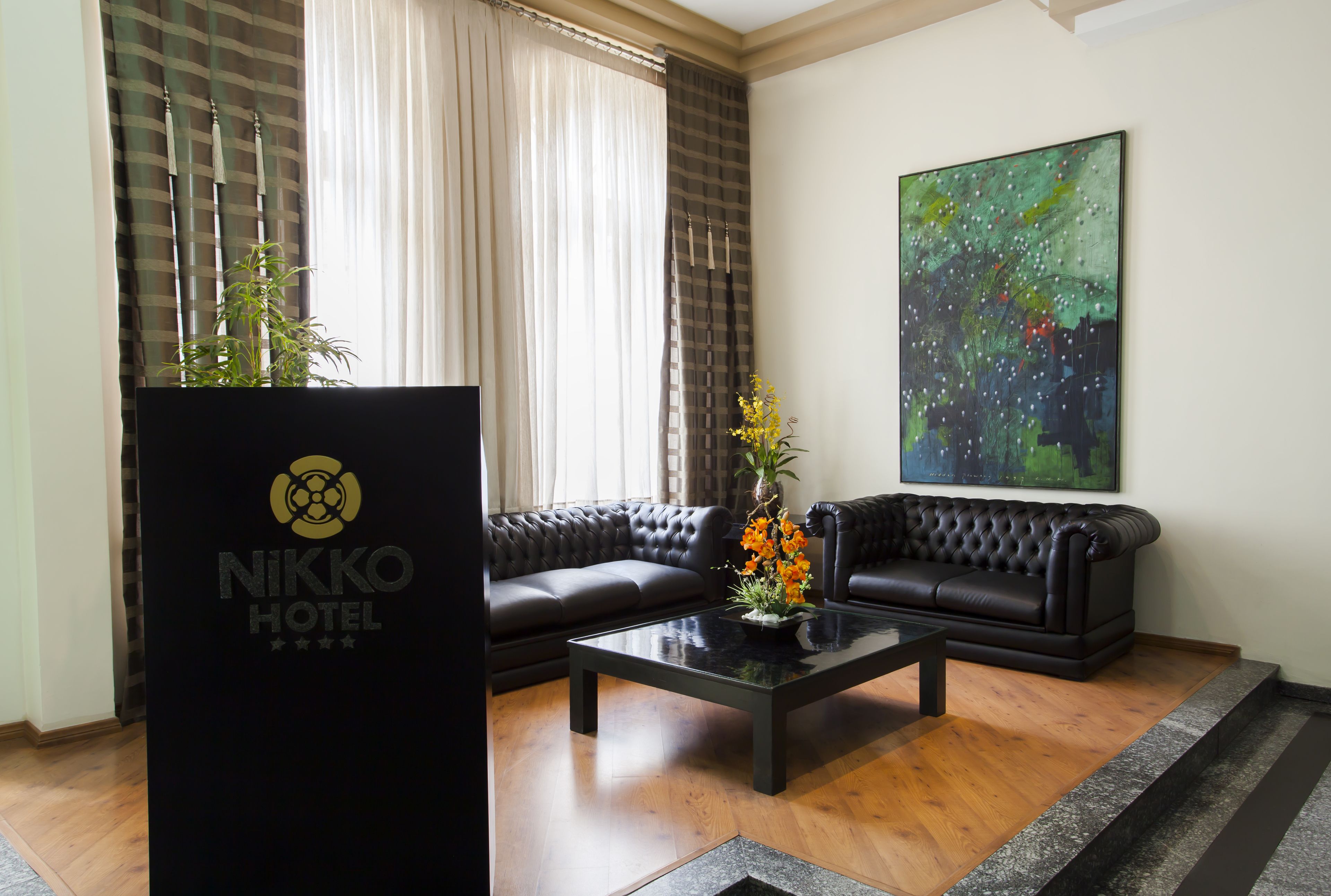 Un hall d’hôtel moderne avec un canapé en cuir noir, une table basse agrémentée d’un arrangement floral et un grand tableau abstrait accroché au mur.