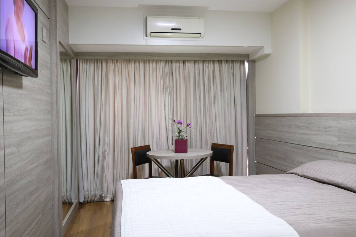 Une chambre d’hôtel comprenant un lit, une petite table avec des chaises, un téléviseur fixé au mur et un appareil de climatisation.