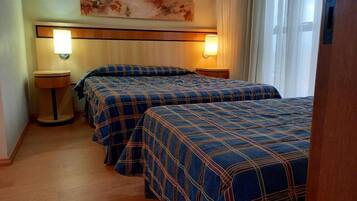 A hotel room with two beds, each with a plaid bedspread, a nightstand with a lamp, and a painting on the wall.