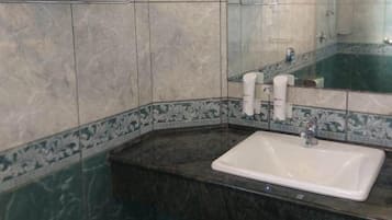 A bathroom with a marble wall, a sink, and a mirror.