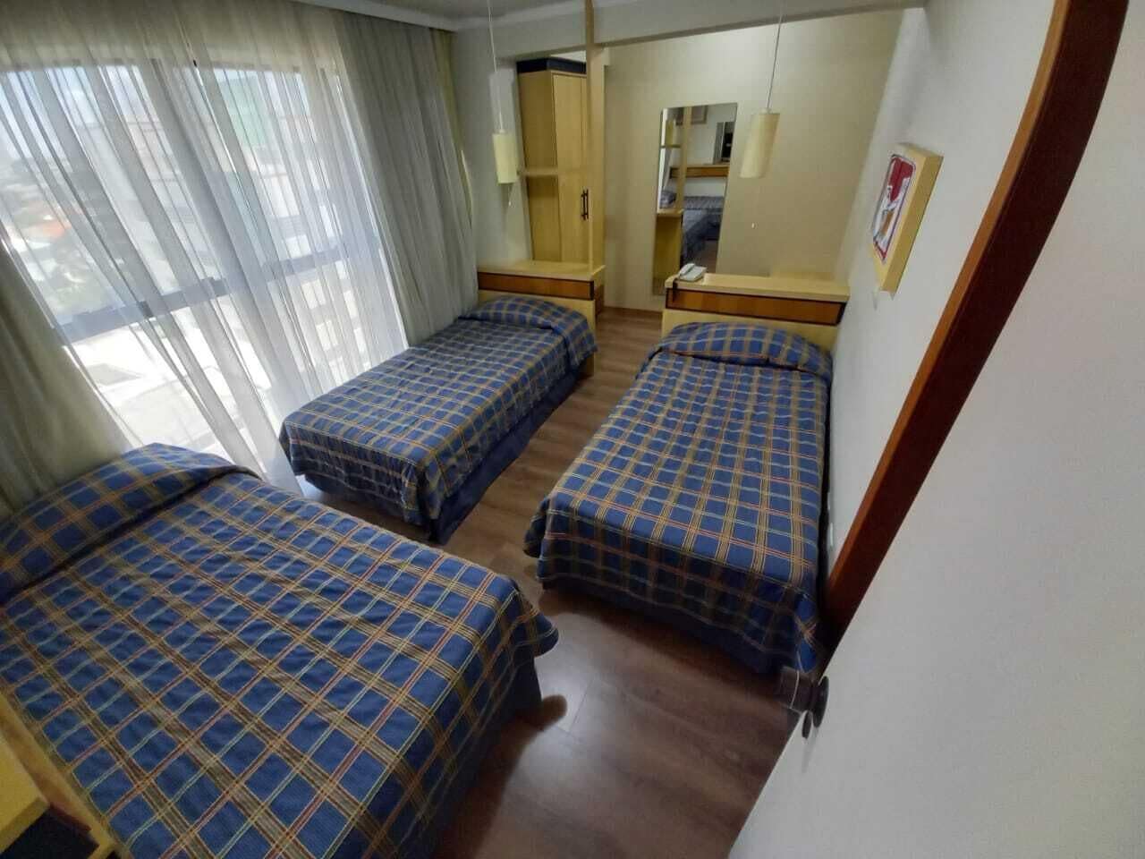 Ein Hotelzimmer mit drei Betten, einem Kleiderschrank, einem Spiegel und einem kleinen Schreibtisch.