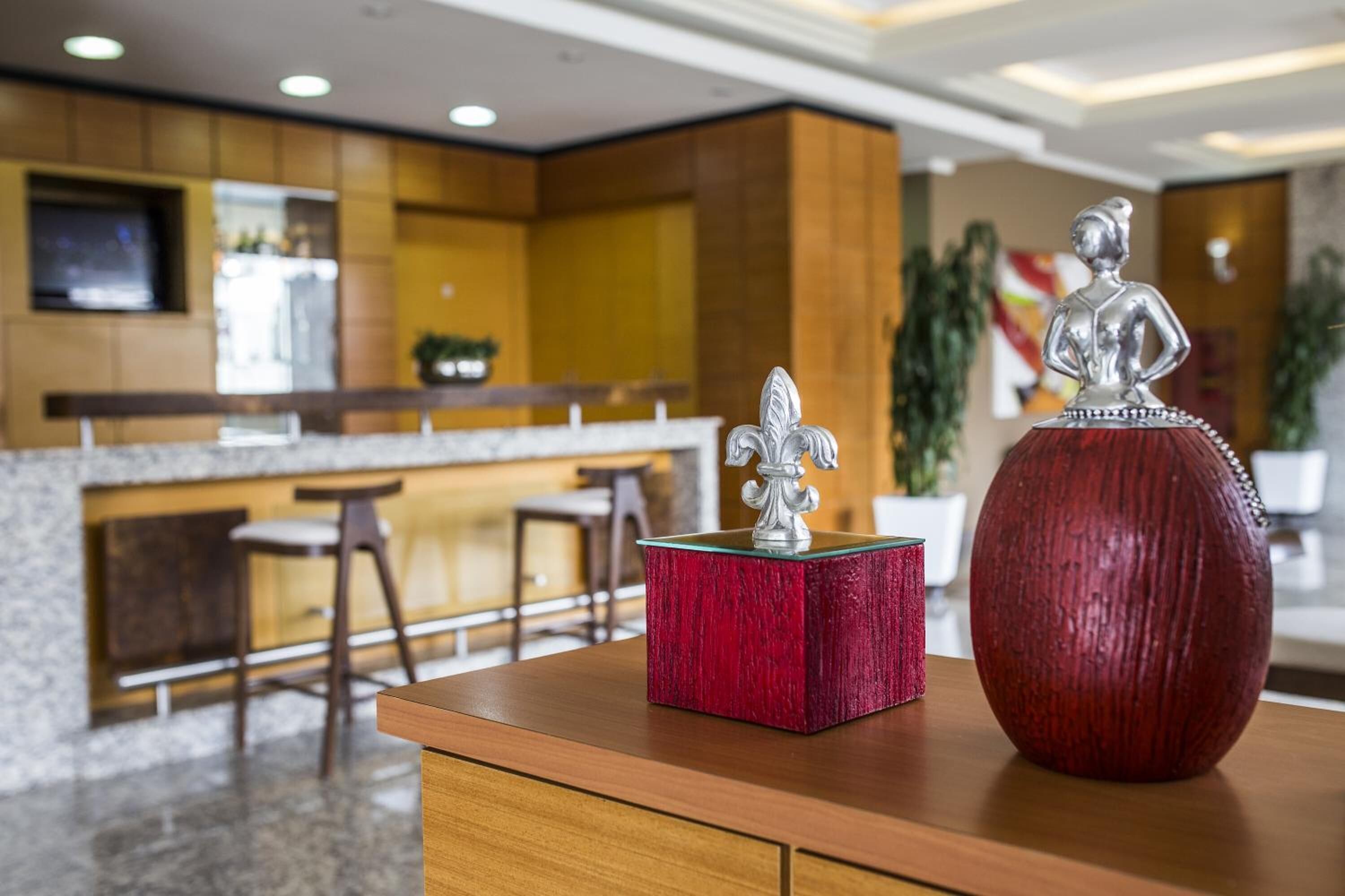 A modern kitchen with a bar area, a red vase, and a decorative silver figure on a wooden table.