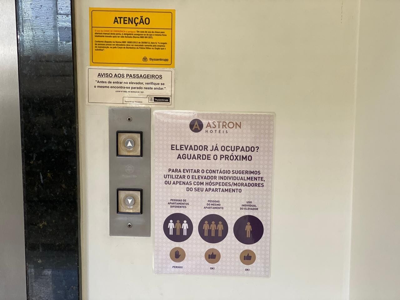 A wall with a yellow attention sign and a poster advising to use the elevator individually or with housekeepers to avoid crowding.
