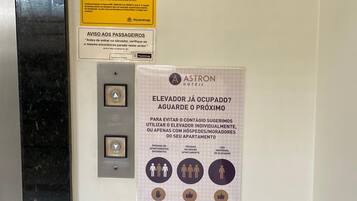 A wall with a yellow attention sign and a poster advising to use the elevator individually or with housekeepers to avoid crowding.