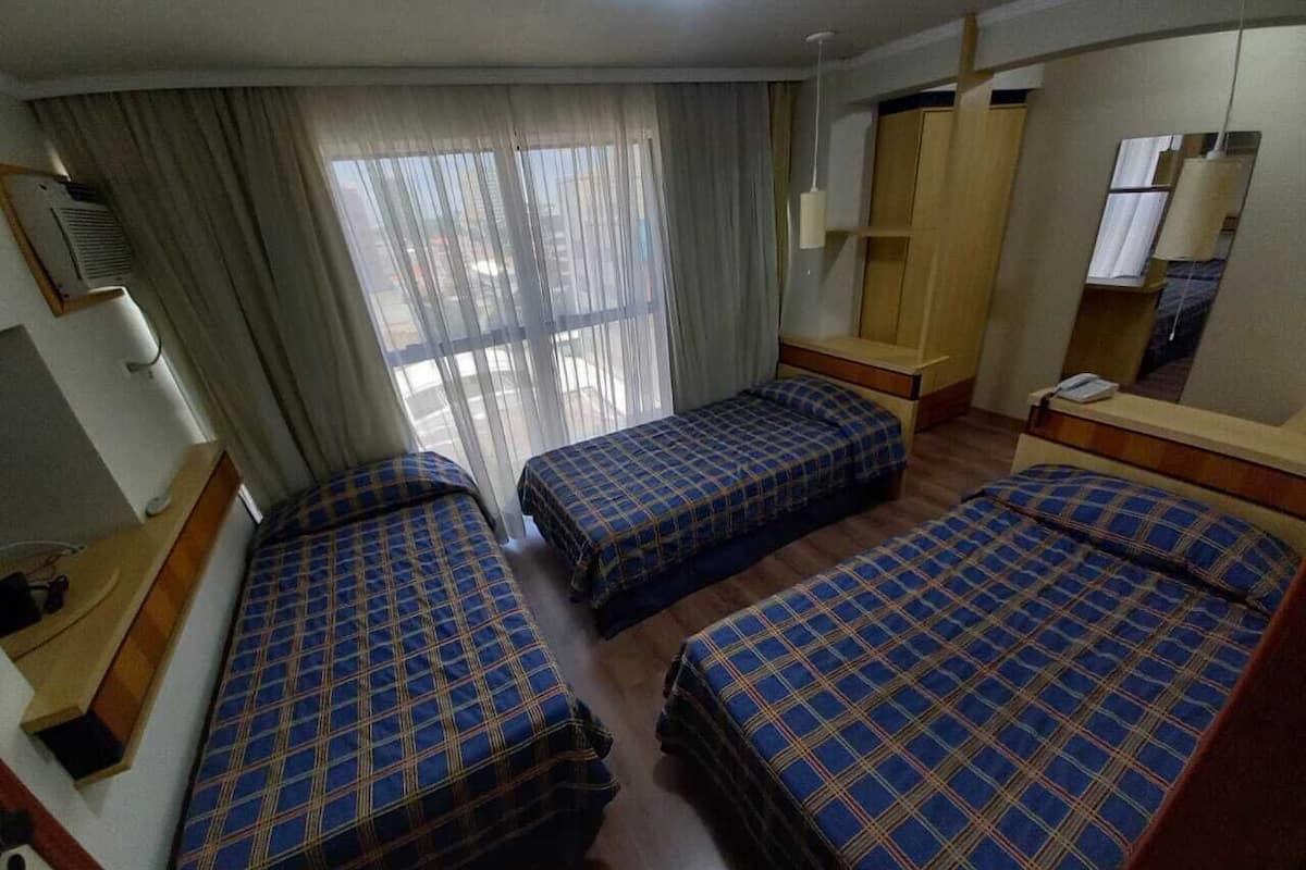 Una habitación de hotel con tres camas, un escritorio, un espejo y una ventana con cortinas.