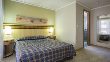 Habitació d'hotel amb un llit gran, dues làmpades de nit, un capçal de llit, un quadre sobre el llit, un mirall a la paret i una porta que dona a una altra habitació.