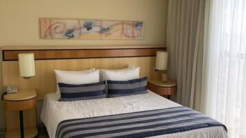 Una habitación de hotel con una cama, dos mesitas de noche, una lámpara de pared y una ventana con cortinas.