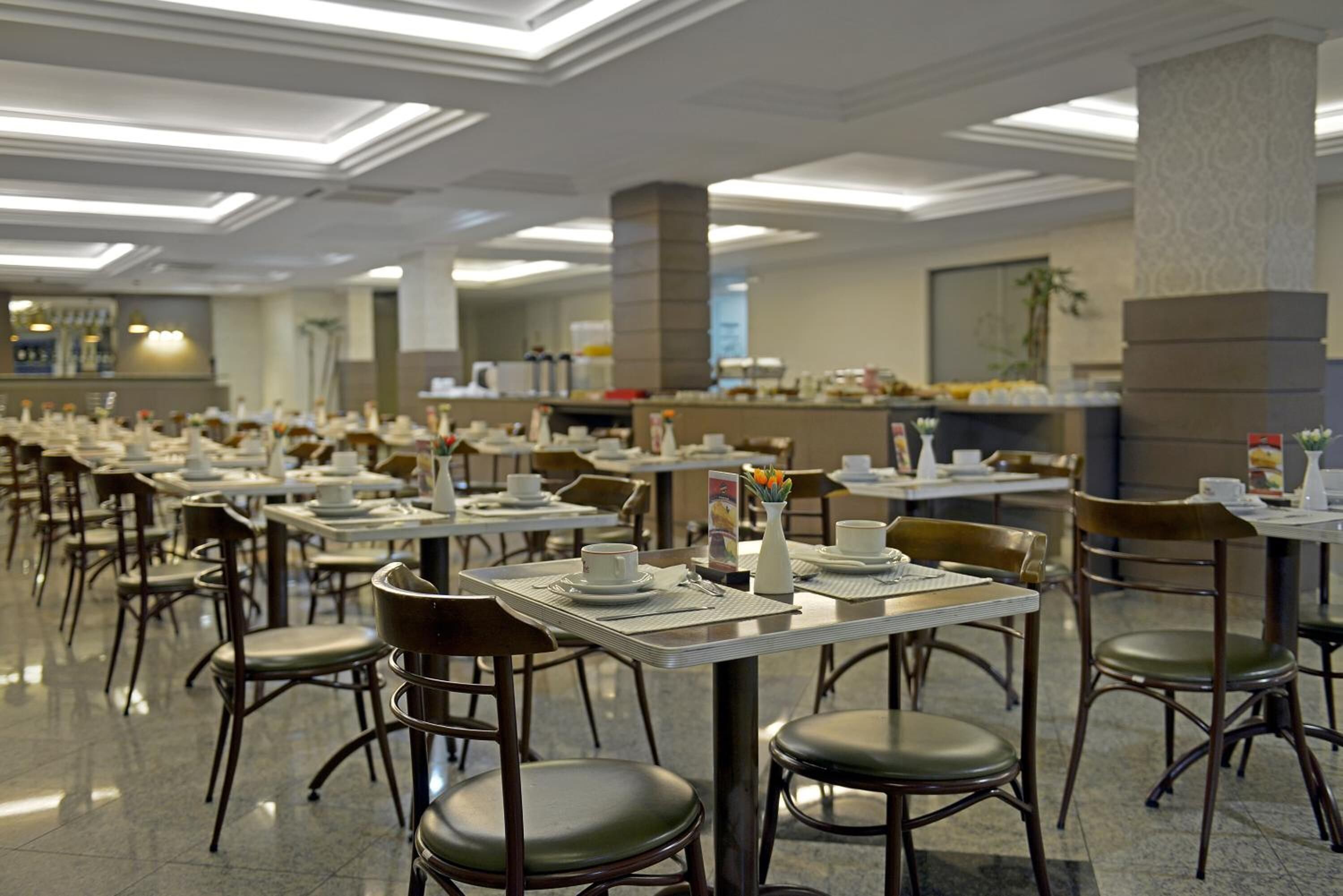A spacious dining area with multiple tables and chairs, a buffet setup, and a modern ceiling design.