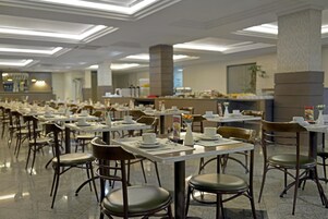 Un amplio comedor con múltiples mesas y sillas, una barra de buffet y un diseño moderno de techo.