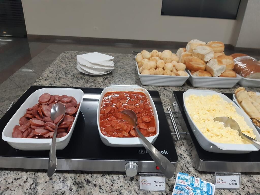 A buffet with various food items including sliced sausages, a red sauce, scrambled eggs, and pastries.