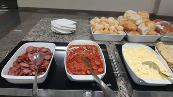 A buffet with various food items including sliced sausages, a red sauce, scrambled eggs, and pastries.