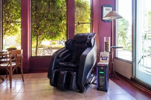 A massage chair in a room with large windows, a table with chairs, and a lamp. - Hotel Flat Petras (Curitiba)