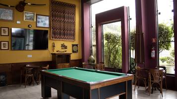 Una sala de billar con mesa de pool, sillas y televisor.