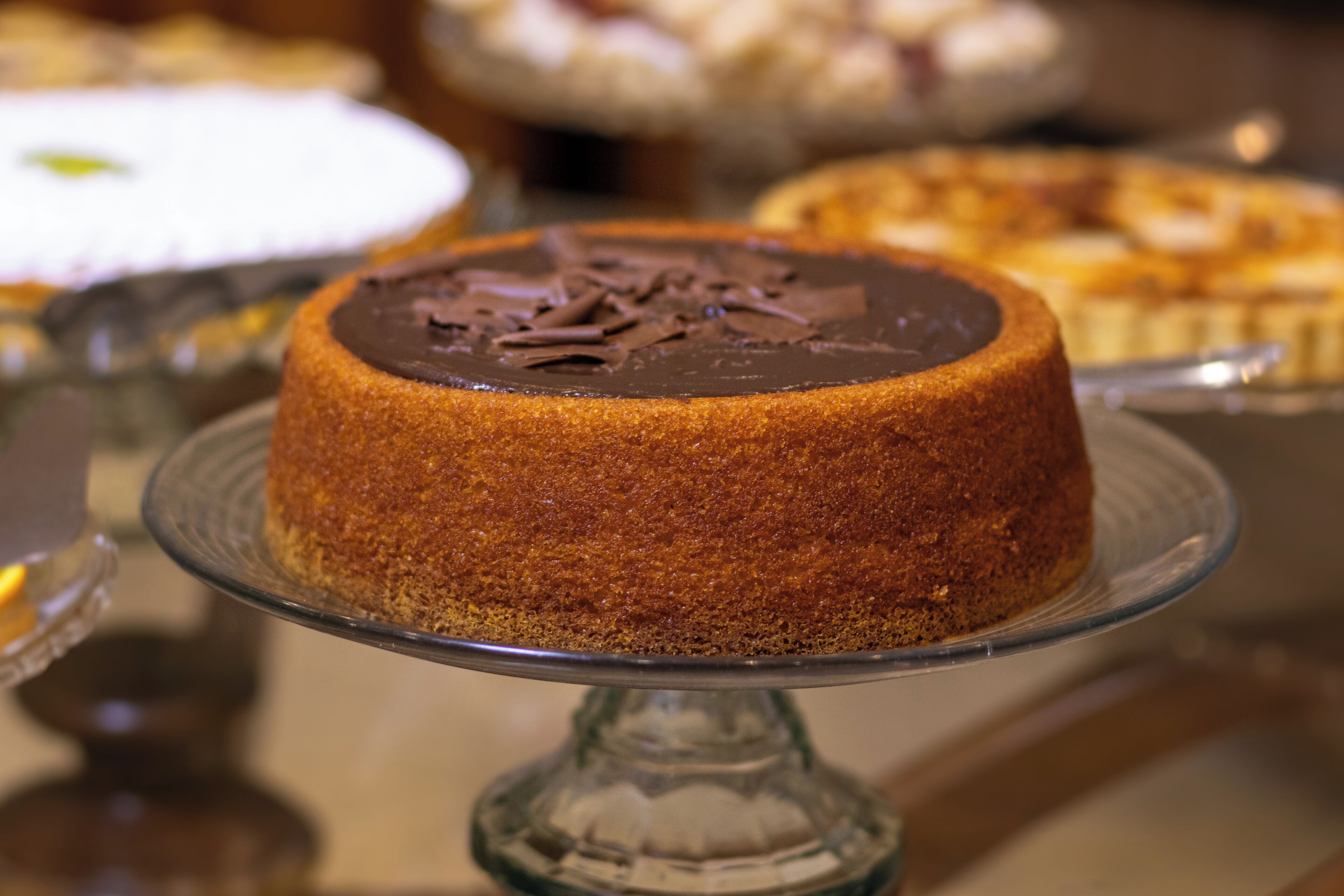 Un pastel sobre un pedestal de vidrio con cobertura de chocolate.