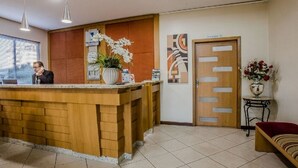 A reception desk with a wooden counter, a potted plant, and a framed abstract artwork on the wall. - Foz Presidente Economic Hotel (Foz do Iguaçu)